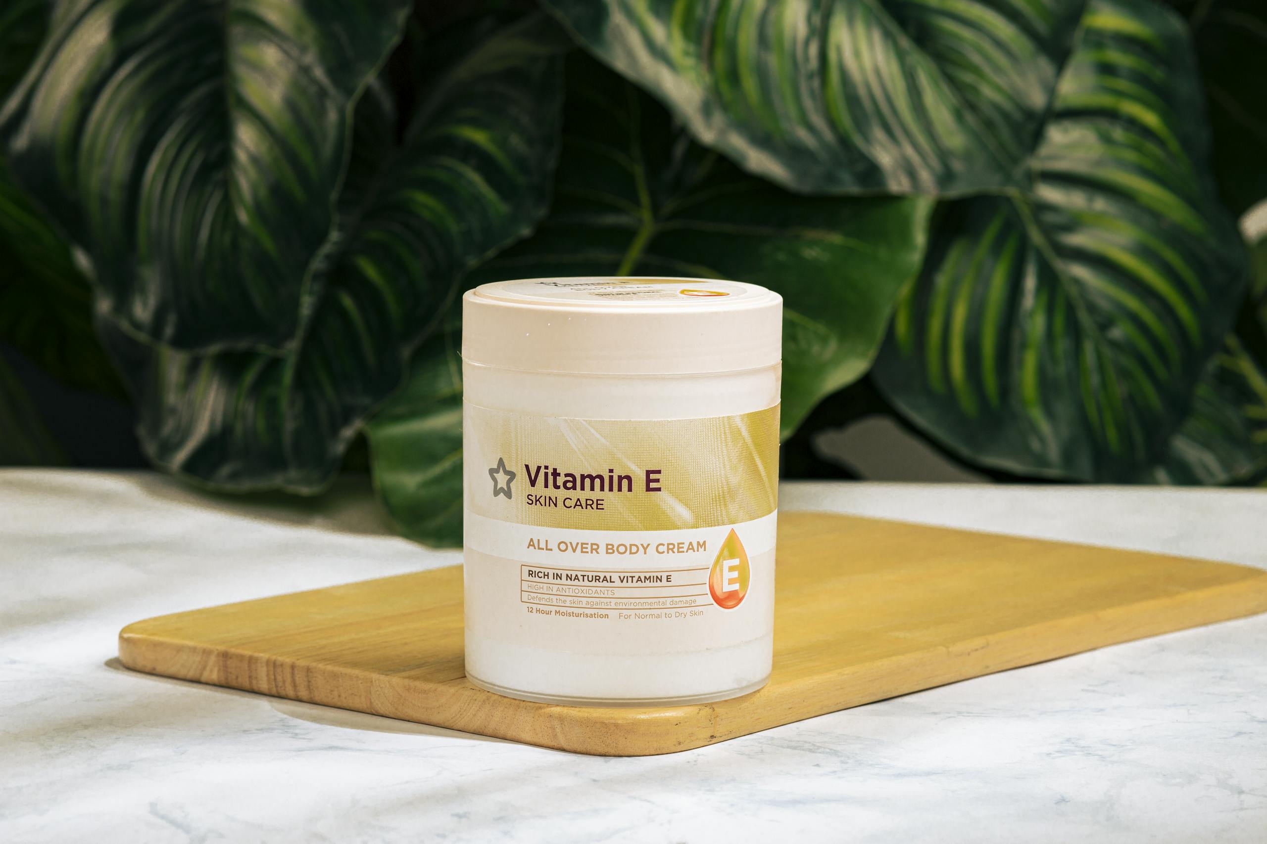 Vitamin E skin care cream on a wooden tray with green foliage background.